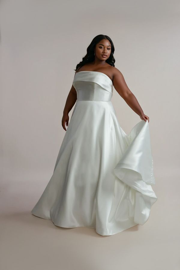 A woman wearing a white satin wedding dress with a strapless neckline, A-line silhouette, and a dramatic train.