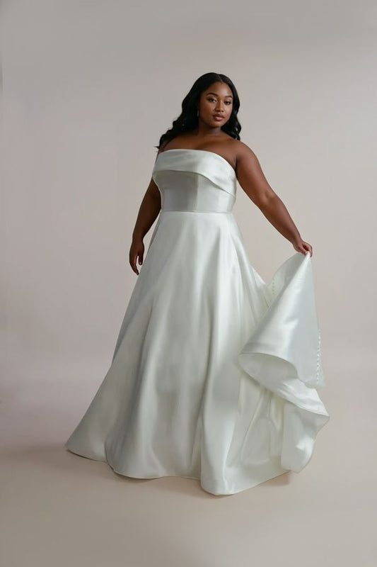 A woman wearing a white satin wedding dress with a strapless neckline, A-line silhouette, and a dramatic train.