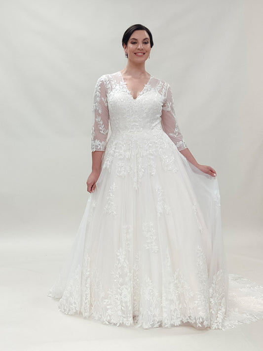 "Plus-size bride smiling in a lace A-line lace wedding dress with long sheer sleeves ."