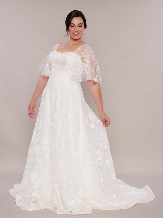 "A bride in an ivory lace wedding dress with a sweetheart neckline, flutter sleeves, and a full A-line skirt extending into a soft train."