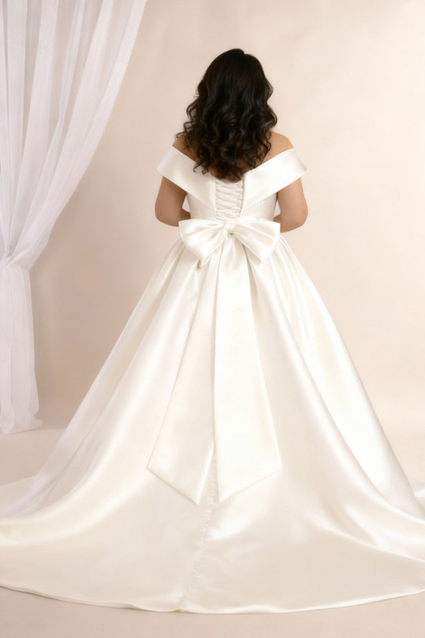 Woman wearing an Ivory satin wedding dress with a bow detail, standing against a plain background.